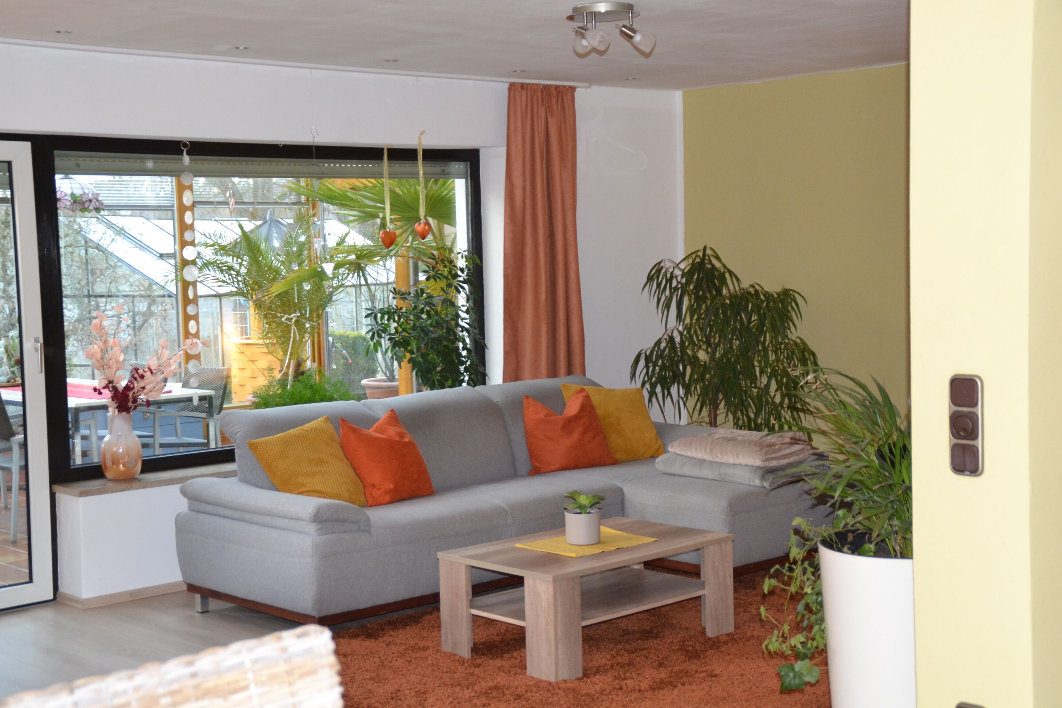 A modern living room with a grey sofa, orange cushions, a wooden coffee table, and potted plants.