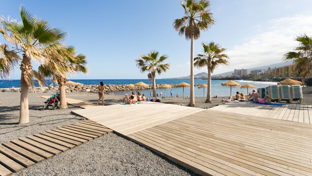 A beach with wooden walkways, palm trees, and umbrellas. - Frontline Duplex Las Arenitas with pool (Candelaria)