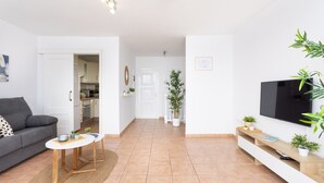A modern living room with a grey sofa, a small round table, a TV, and a kitchen in the background. - Frontline Duplex Las Arenitas with pool (Candelaria)