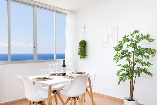 A dining area with a table set for two, a bottle of wine, and a view of the sea through large windows.