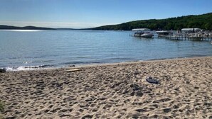 Uma praia com areal, um lago calmo e um cais com barcos.