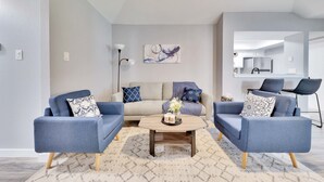 Un salon moderne avec deux fauteuils bleus, un canapé beige et une table basse agrémentée d’objets décoratifs.