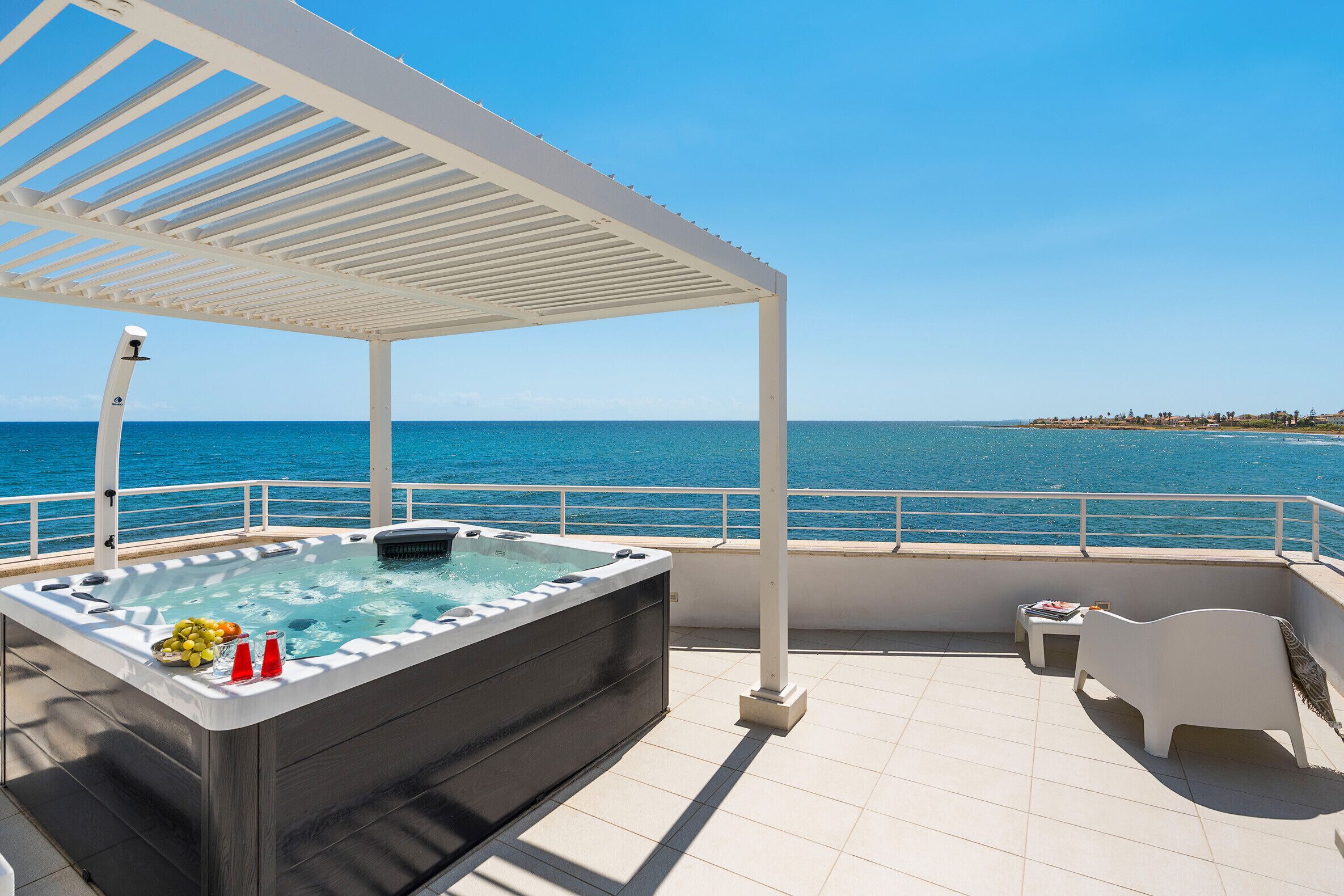 Een terras op het dak met een jacuzzi, een tafel met drankjes en uitzicht op zee.