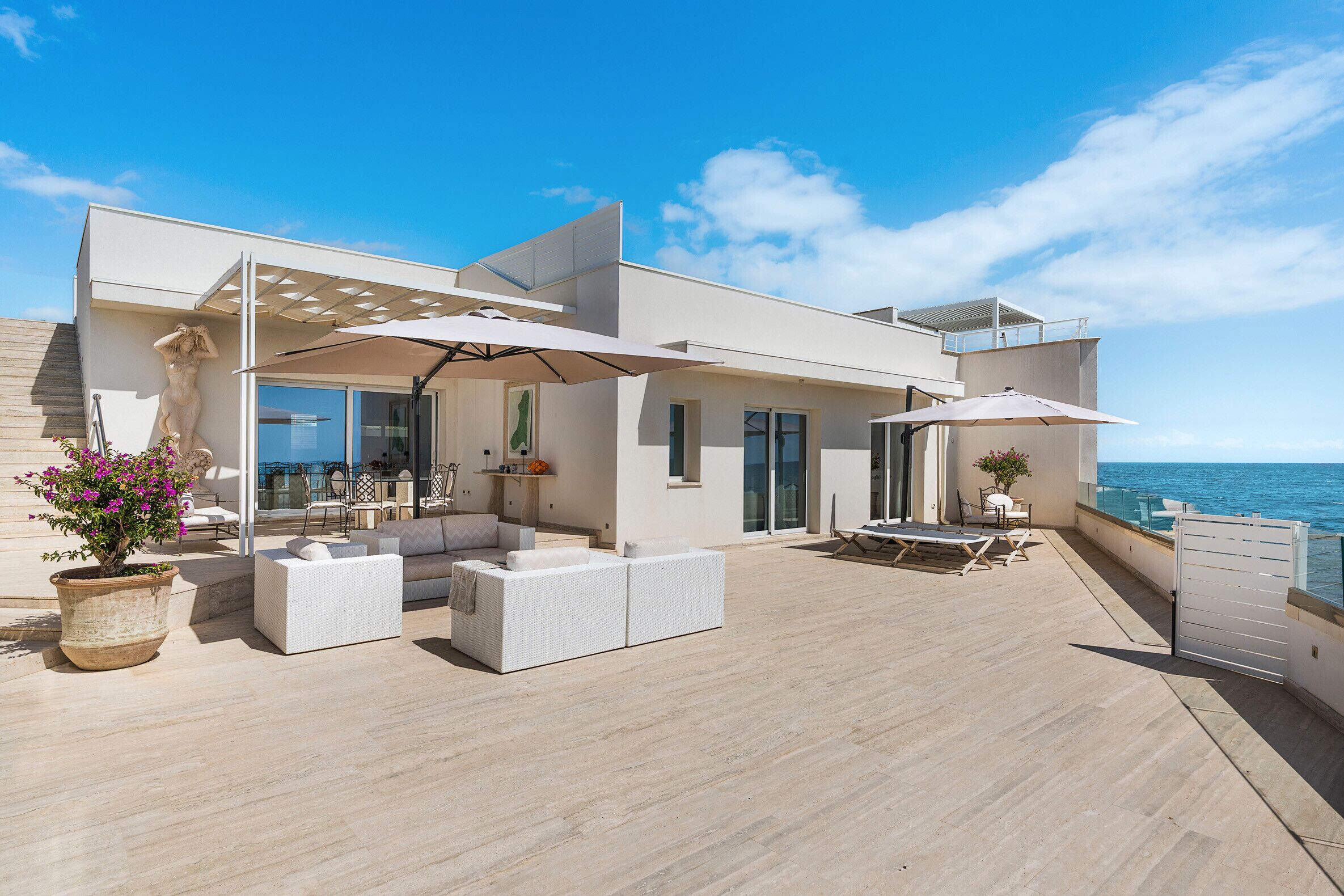 Un espace de vie extérieur moderne, doté d’une piscine, de coins salon et offrant une vue sur la mer.