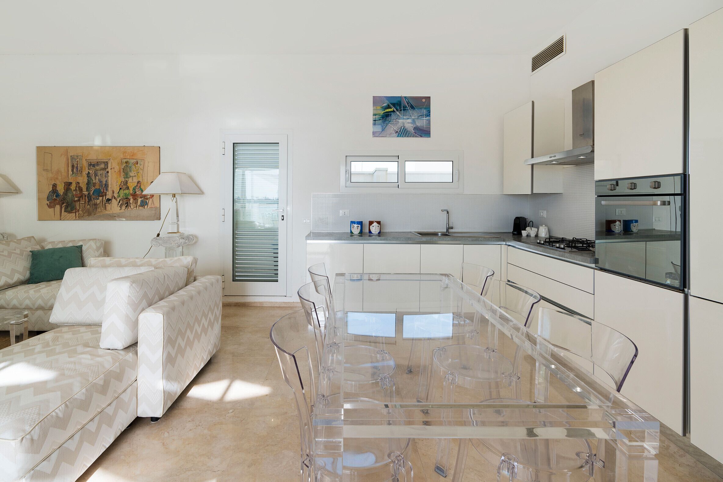 A modern kitchen with a large dining table, clear chairs, and a built-in oven.