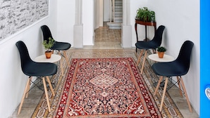 A hallway with a patterned rug, black chairs, a staircase, and a white wall with a textured design. - San Fransisco Studios Valletta (Floriana)