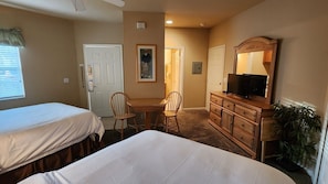 A hotel room with two beds, a desk, a television, and a mirror.