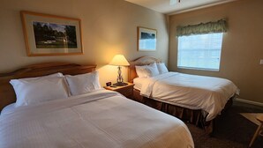 Ein Hotelzimmer mit zwei Betten, einem Nachttisch mit Lampe, einem gerahmten Bild an der Wand und einem Fenster mit Vorhang.