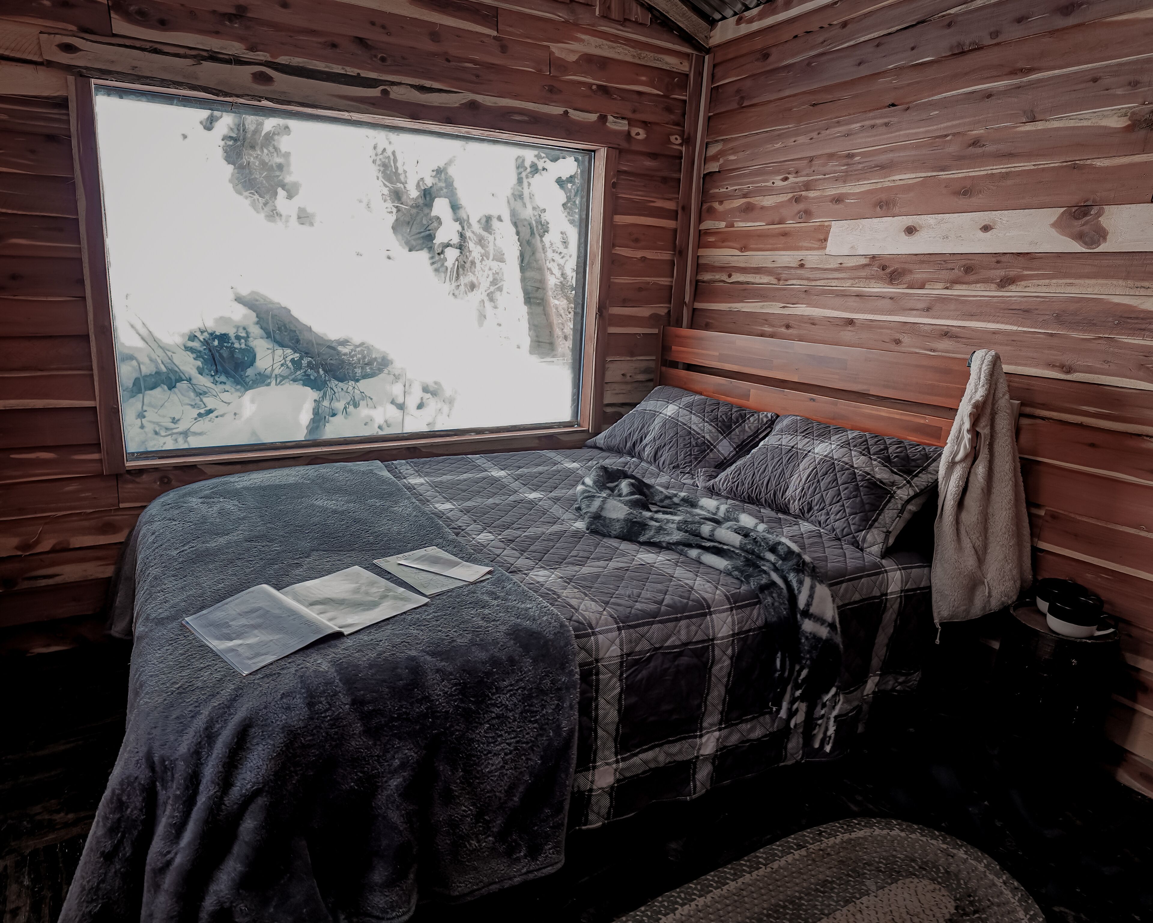 Una habitación cálida tipo cabaña con un ventanal grande, una cama con manta escocesa y una toalla colgada en la pared.