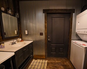A bathroom with a double sink, a mirror, a towel rack, a door, and a white washing machine. - Glamping Cabin | Huge Window | Cliff and Animal Views (Green Township)