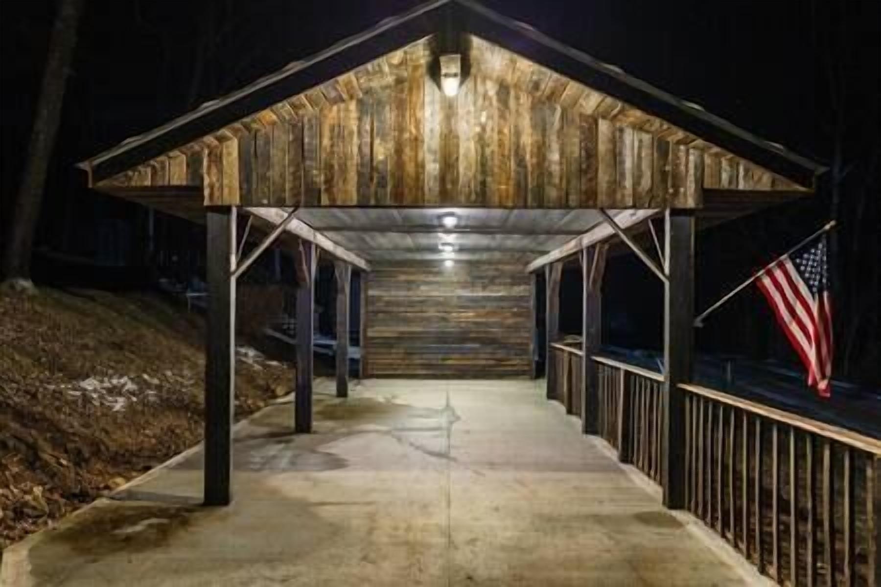 A covered outdoor area with a concrete floor, wooden walls, and a metal railing.