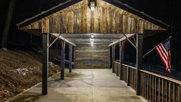 A covered outdoor area with a concrete floor, wooden walls, and a metal railing.