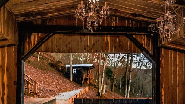 A wooden covered structure with a wooden deck and stairs leading to a small cabin.