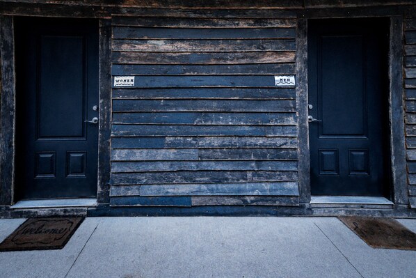 A building facade with two closed doors, each marked with a sign indicating "WOMEN" and "MEN".