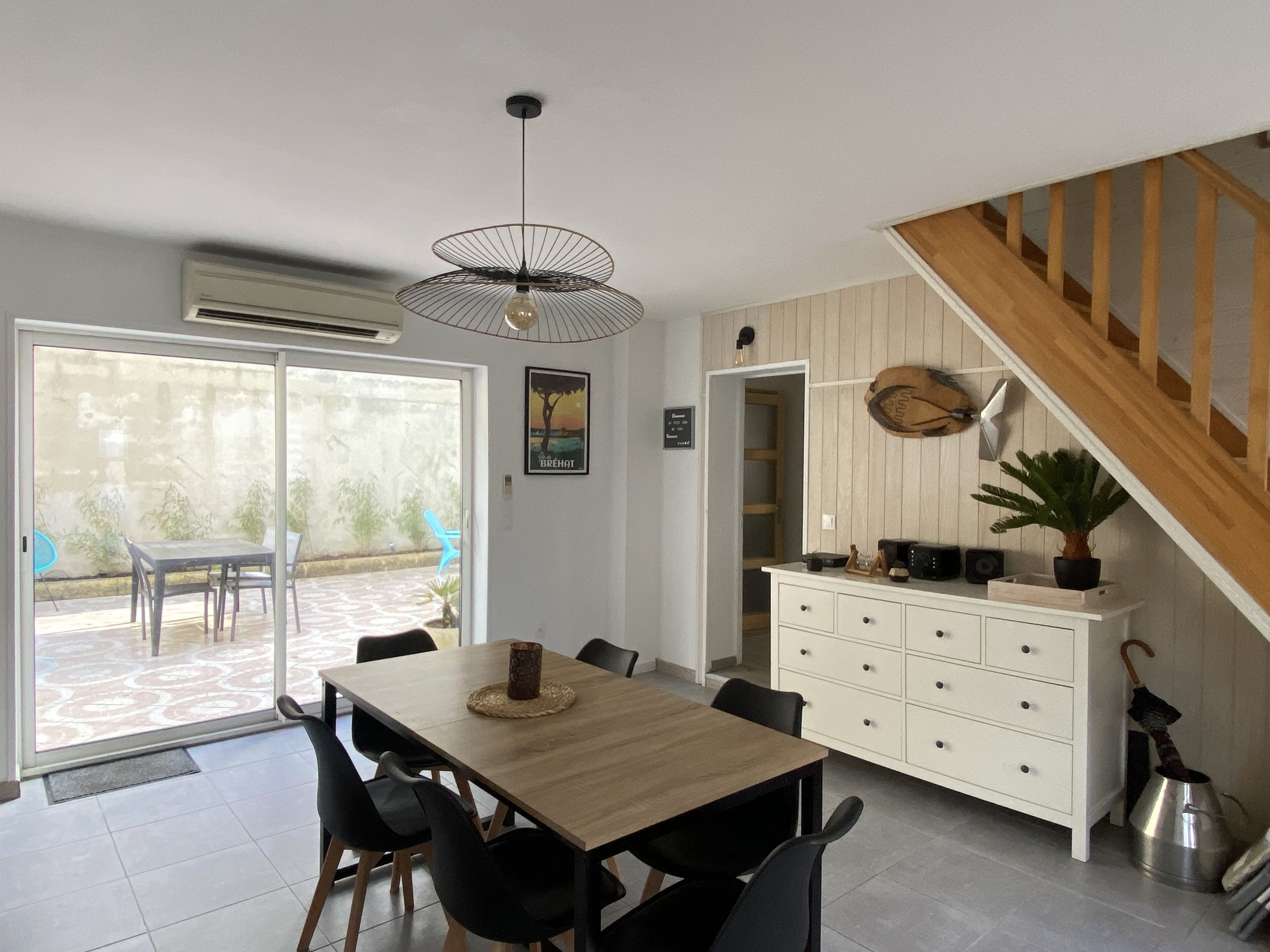 Un coin repas avec une table et des chaises en bois, un meuble blanc avec des tiroirs et un escalier menant à un autre niveau.