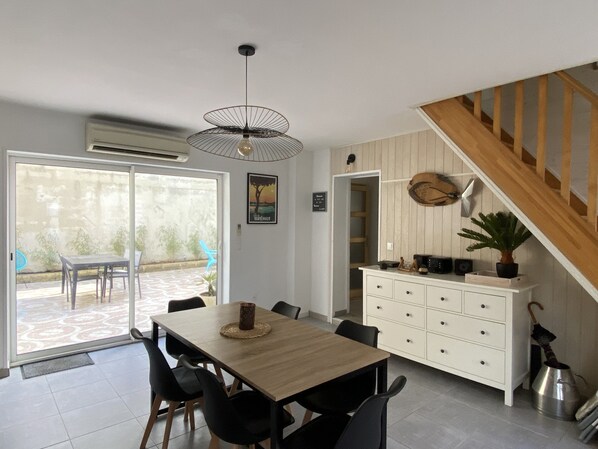 A dining area with a wooden table and chairs, a white cabinet with drawers, and a staircase leading to another level. - Petit Coin du Port (Ploubazlanec)