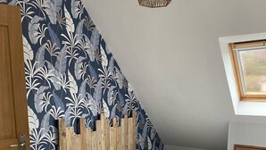 A bedroom with a sloped ceiling, a bed with white bedding, a wooden headboard, and a wall with a leaf-pattern wallpaper.