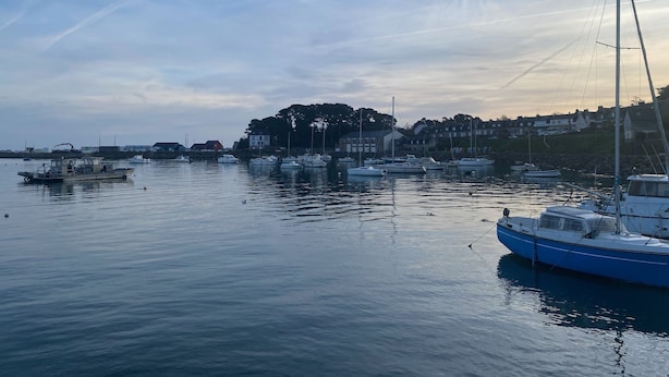 A harbor with boats docked, calm water, and buildings in the background.