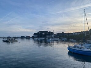 A harbor with boats docked, calm water, and buildings in the background. - Petit Coin du Port (Ploubazlanec)