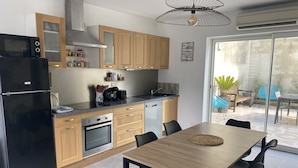 A modern kitchen with wooden cabinets, a black refrigerator, a built-in oven, and a dining area with a wooden table and black chairs.