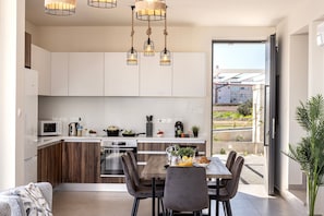Une cuisine moderne avec des meubles en bois, un coin repas comprenant une table et des chaises, et une vue dégagée par une porte ouverte.