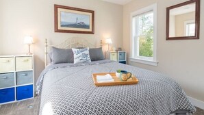 Een slaapkamer met een bed, nachtkastje, dressoir, raam en een fotokader aan de muur.