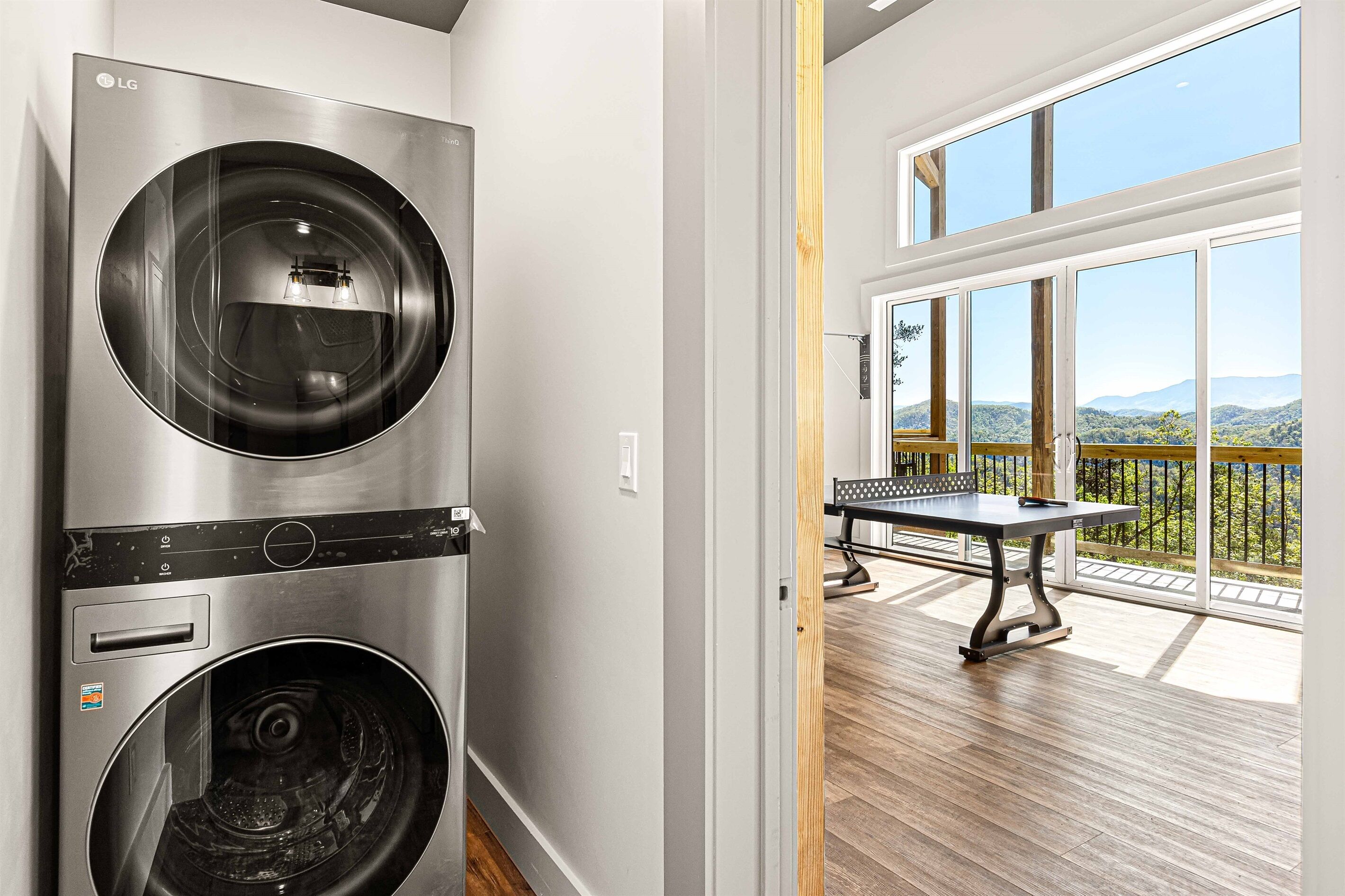 A laundry area with stacked washers and dryers, a wooden deck with a table, and a balcony with a view.