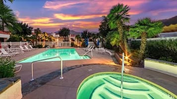 A swimming pool with lounge chairs and palm trees, surrounded by buildings.