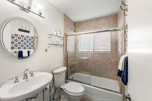 Een badkamer met een wastafel, toilet en douchecabine met raam.