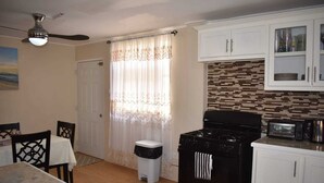 A compact kitchen with a stove, microwave, and cabinets. There's a dining table with chairs and a trash bin. - Belle Zoon Villa (Gros Islet)