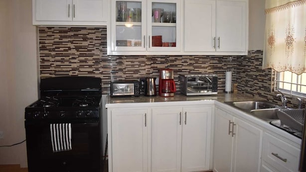 A compact kitchen with white cabinets, a black stove, a toaster, a coffee maker, and a microwave. - Belle Zoon Villa (Gros Islet)