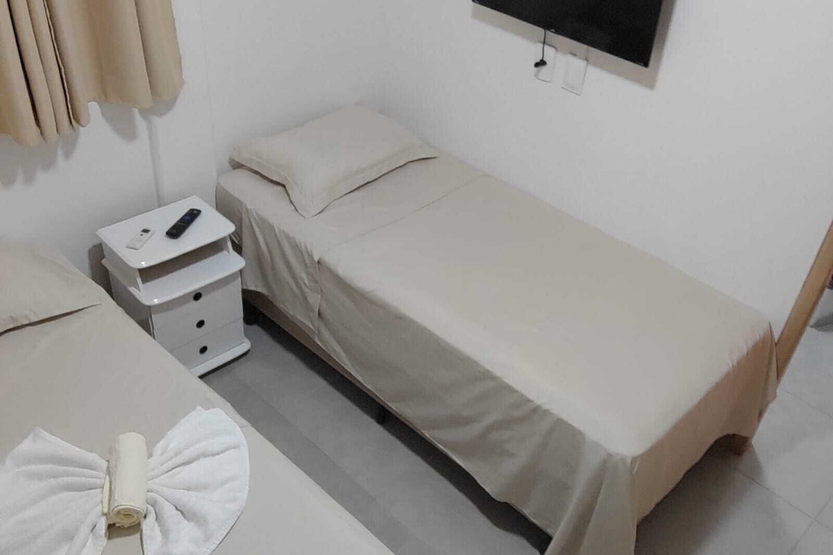 A small, clean room with two beds, a TV, and a bedside table with a remote control.
