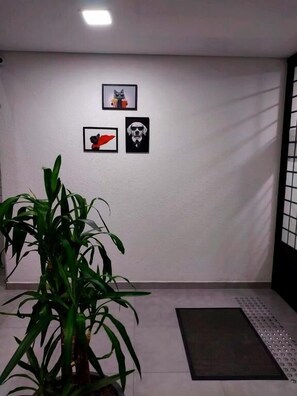 A room with a white wall, three framed pictures, a potted plant, and a mat on the floor. - pousada São José (Joinville)