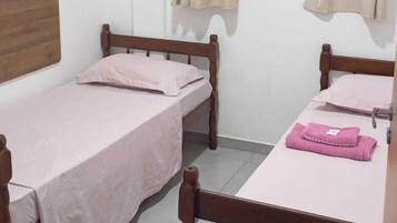 A dormitory room with two single beds, a wooden headboard, a window with curtains, and a tiled floor.