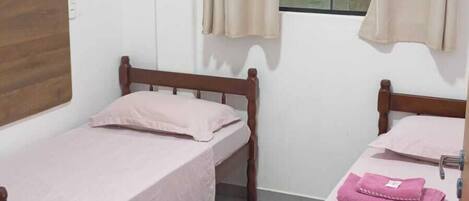 Quarto de estudante com duas camas individuais, cabeceira de madeira, janela com cortinas e chão de azulejos.