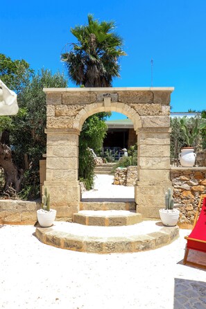 A stone archway leading to a courtyard with potted cacti and a palm tree. - Prossimante disponibile Splendida struttura luxury Trullo e Pajara  (Capilungo)