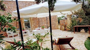 Eine Terrasse im Freien mit Steinböden, weißen Möbeln und Sonnenschirmen.