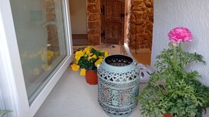 Ein Flur mit Steinwänden, einer Holztür, einem Blumentopf mit gelben Blüten und einem dekorativen Keramiktopf.