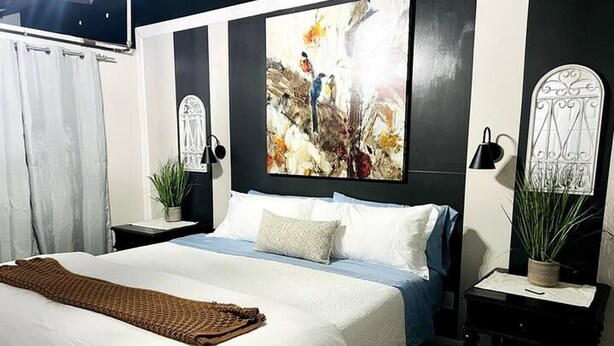 Une chambre avec un grand lit, un tableau au mur et deux tables de chevet ornées de plantes.