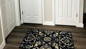 Un couloir avec deux portes blanches, un tapis à motifs sombres et un plancher en bois.