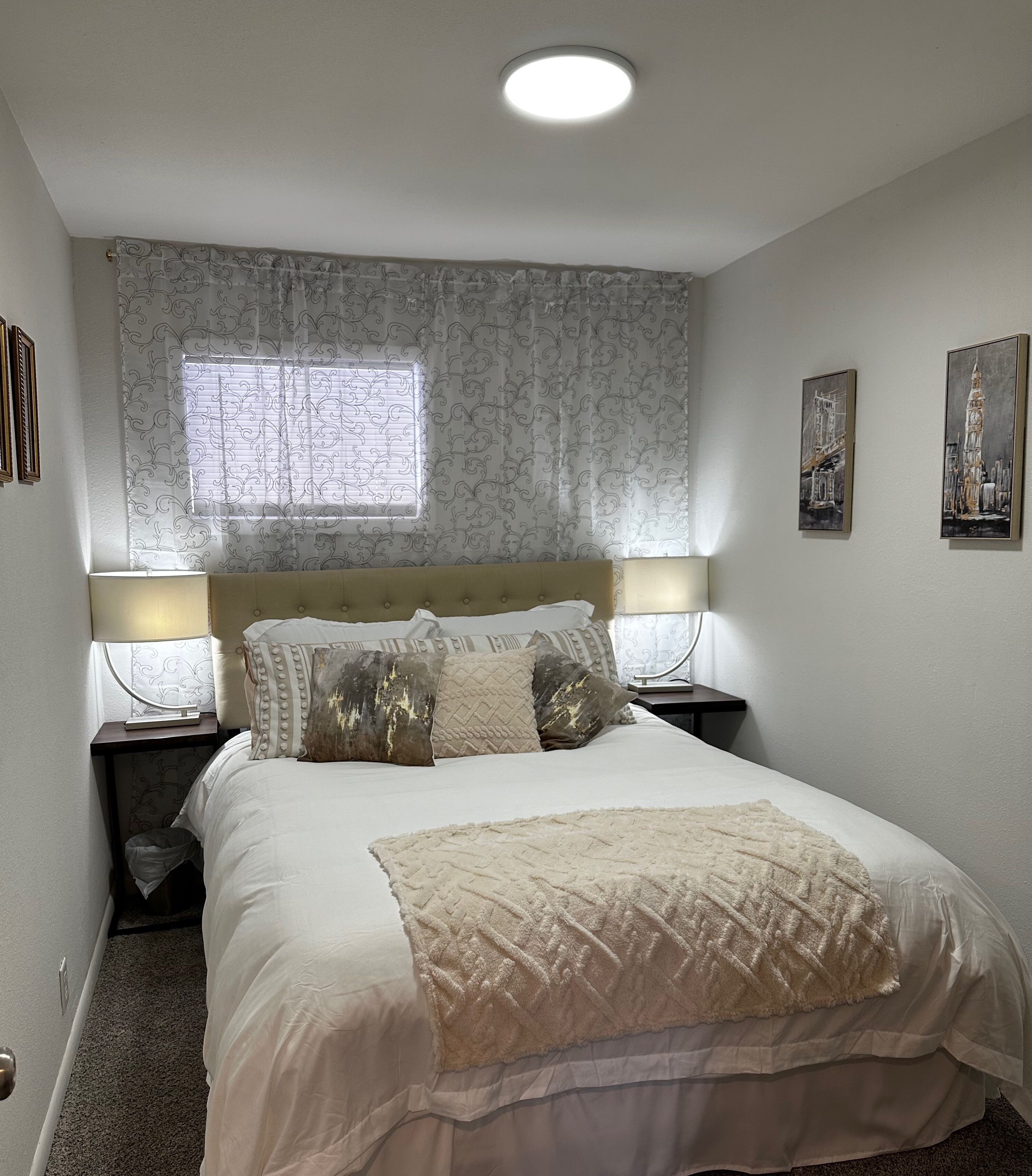 A bedroom with a bed, two bedside tables, a window with curtains, and wall art.