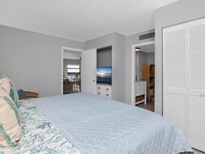 Une chambre à coucher comprenant un lit, une télévision, une armoire et donnant sur l’extérieur.