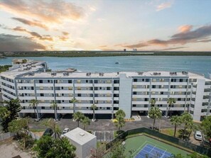 A multi-story hotel with a curved facade, a rooftop pool, and a tennis court.