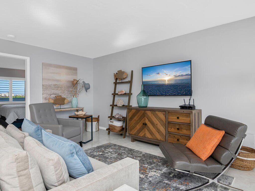 Una sala moderna con un sofá gris, un sofá de cuero marrón y un sillón gris. Se observa un mueble de madera con cajones y un televisor montado en la pared.