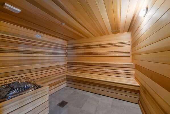 Una sala de sauna con listones de madera en paredes y techo, un banco y un estante de metal.
