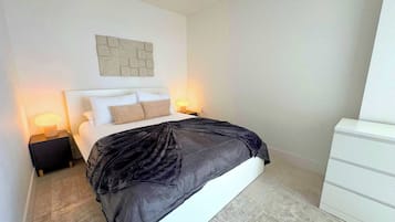 A modern bedroom with a bed, two bedside tables with lamps, a headboard, a wall-mounted artwork, and a white dresser.