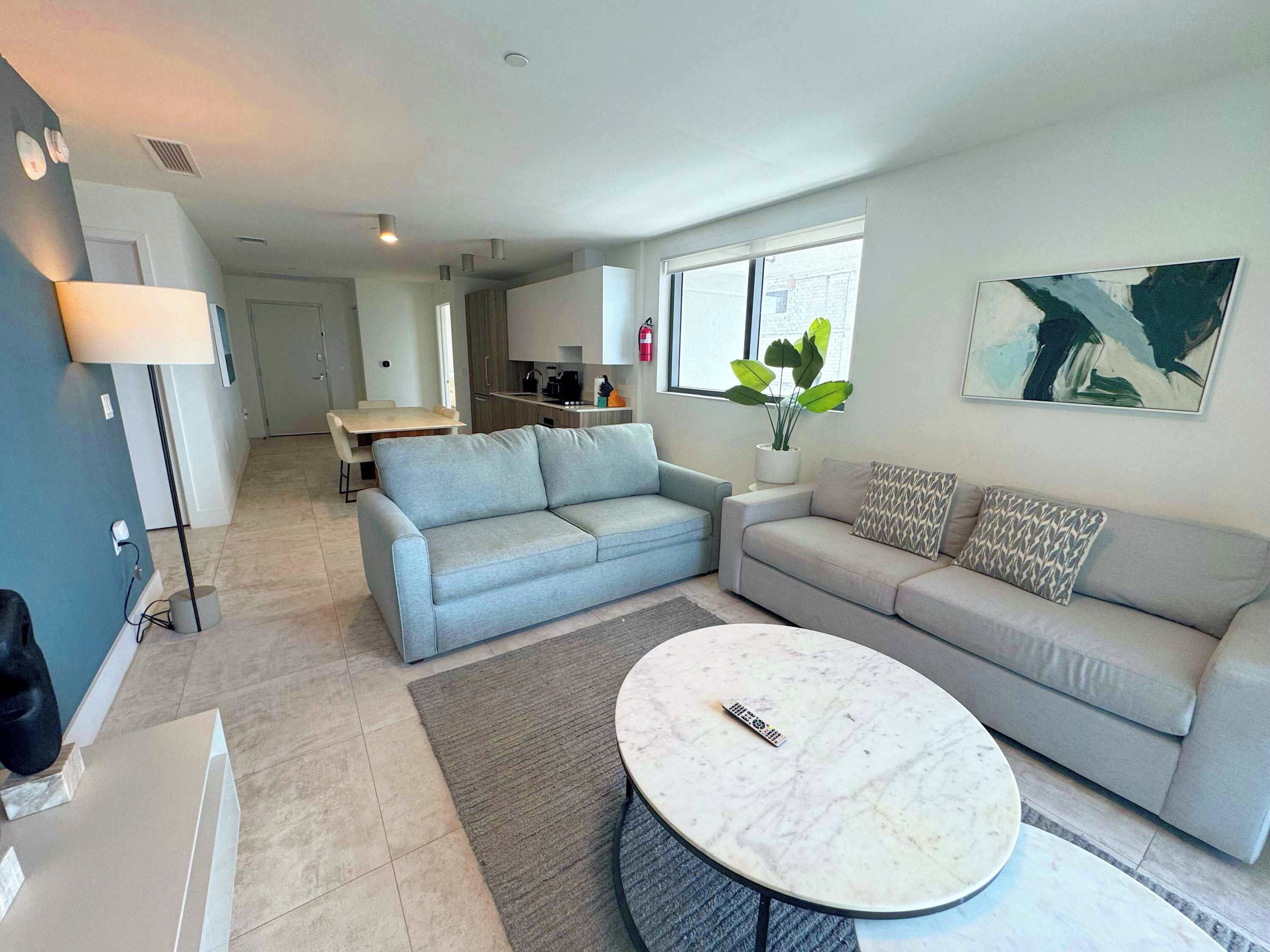 A modern living room with a grey sofa, a round coffee table, and a dining area in the background.