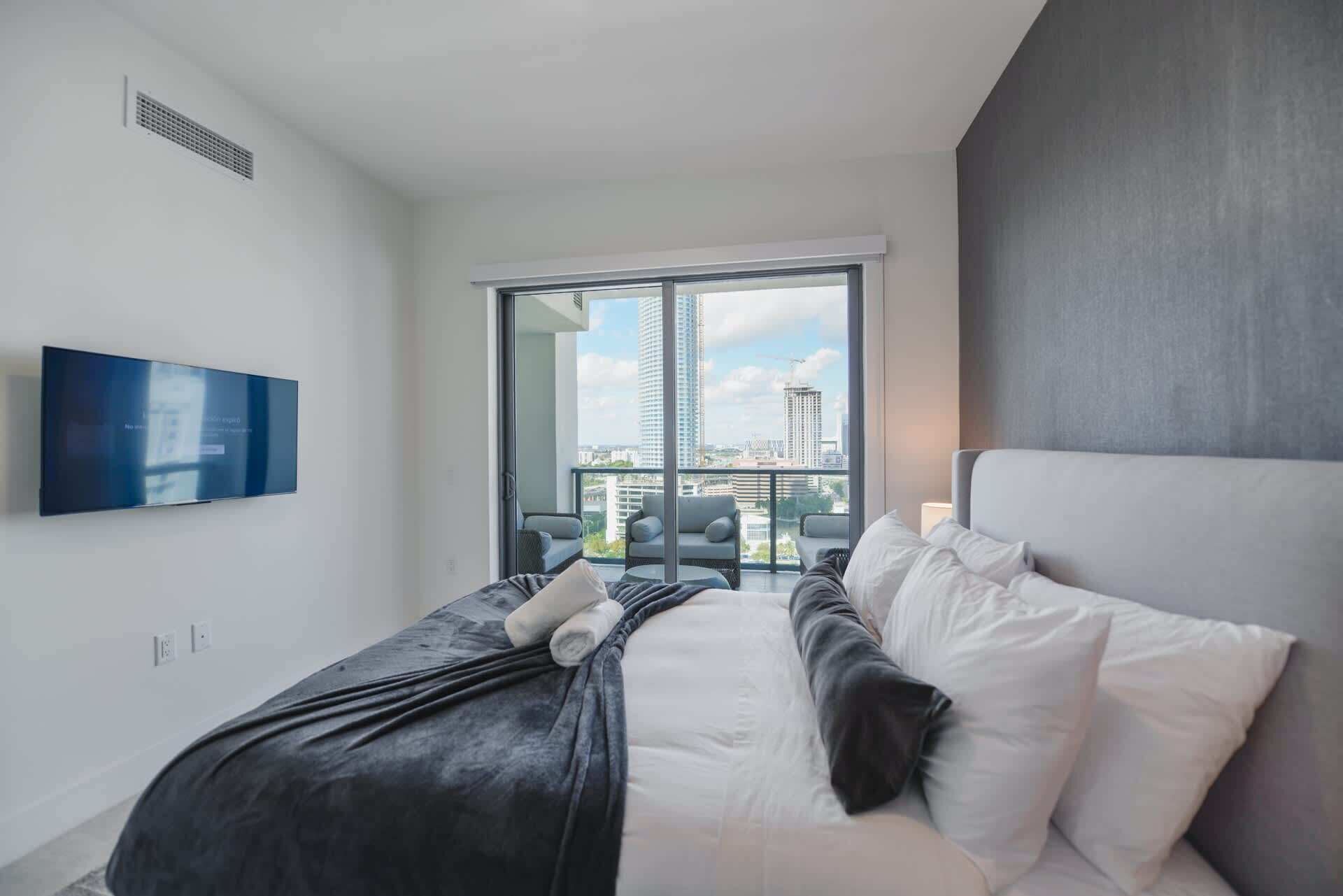 Una camera d'albergo moderna con un letto grande, una televisione a schermo piatto montata sulla parete e un balcone con vista sulla città.