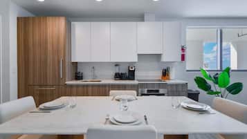 A modern kitchen with white cabinets, a dining table set for four, and a view of the outdoors through a window.