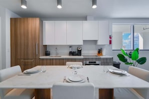 Une cuisine moderne avec des meubles blancs, une table à manger dressée pour quatre personnes et une vue sur l’extérieur par une fenêtre.